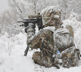 Winter sniper covered in snow and using a tripod to steady the assault rifle