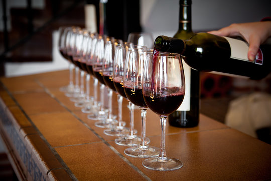 Fototapeta hand with wine bottle filling a row of glasses for tasting