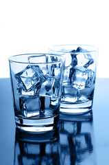 Glasses with crystal clear ice cubes on glossy background