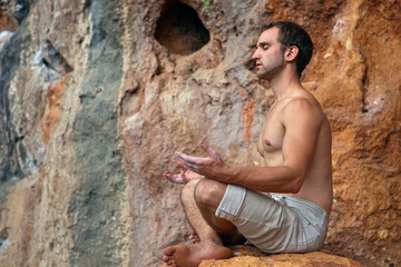 Young man meditating on rock in the mountains