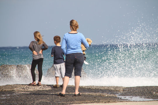 Mutter mit Kindern und Teddy blicken auf die Brandung am Meer