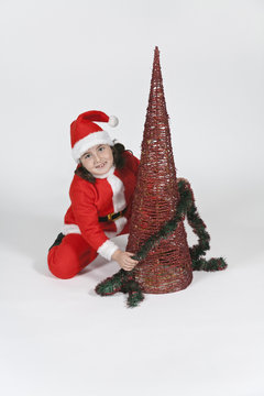 ni&ntilde;o vestido de santa claus decorando el arbol de navidad