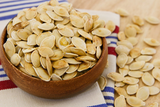 Toasted pumpkin seeds overflowing a wooden bowl