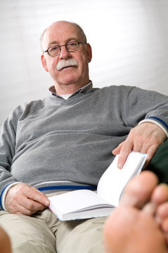 Senior man reading book while sitting on couch