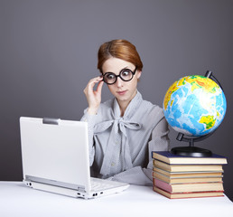 The young teacher in glasses with books, globe and notebook.