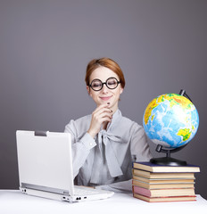 The young teacher in glasses with books, globe and notebook.