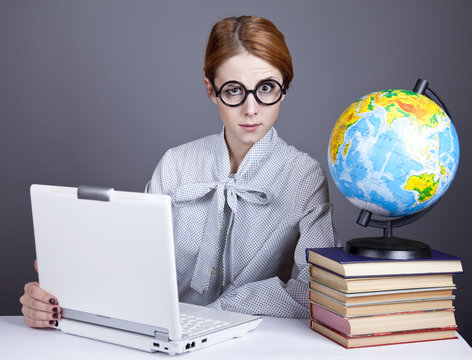 The young teacher in glasses with books, globe and notebook.