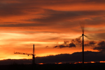 Windrad und Baukran bei Sonnenuntergang