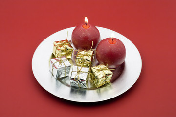 Kerzen mit goldenen und silbernen Päckchen auf Teller