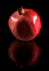 pomegranate; whole fruit isolated on black reflective surface;
