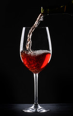 Pouring red wine into a glass over black background