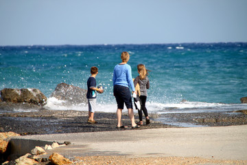 Mutter mit spielenden Kindern mit Ball und Teddy am Meer