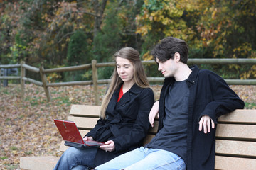Couple looking at latpop on a park bench