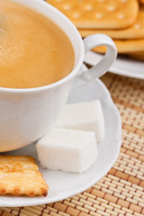 A cup of coffee with a lump sugar and crackers for breakfast
