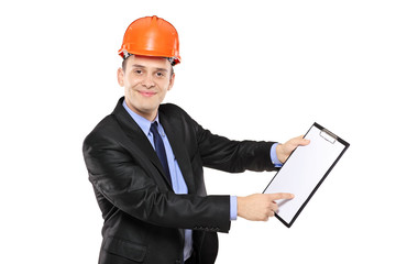 Young foreman wearing helmet and pointing on a clipboard