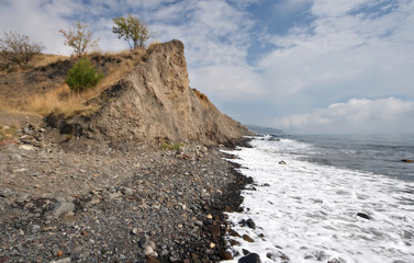 Fototapeta na wymiar Sea coast with pebbles and rock against the sky