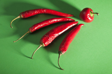 Four red spicy peppers in front of green background