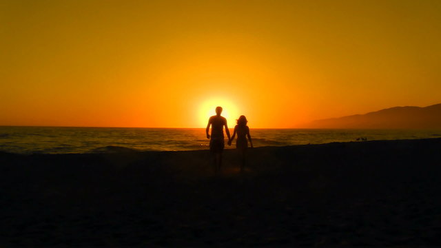 Young couple holds hands walks into sunset - HD