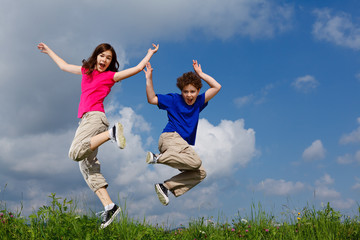 Girl and boy jumping, running against blue sky