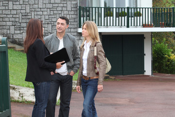 Couple and real-estate agent in front of house for sale