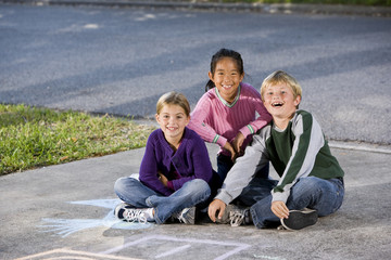 Three happy children sitting on driveway