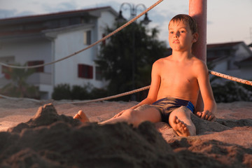 pensive boy after bath sits in sand on beach at evening © Pavel Losevsky