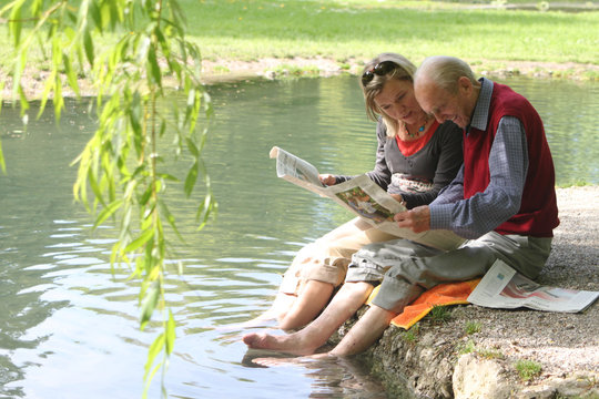 Gro&szlig;vater und Enkelin beim Zeitung lesen am Teich im Gr&uuml;nen