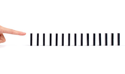Finger ready to push dominoes in a row to cause chain reaction