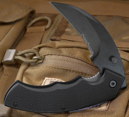 Folding tactical knife with black handle on a tan backpack