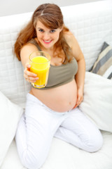 Smiling pregnant woman on sofa with glass of juice. Close-up.