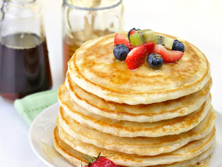 stack of pancakes with maple syrup,honey and berries