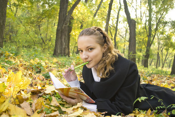 Teen girl lies in autumn park with her diary
