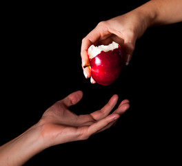 Woman hand giving an apple to man on black background
