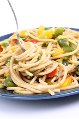 Spaghetti with vegetables being eaten with a fork on white
