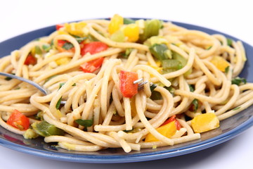Spaghetti with vegetables being eaten with a fork on white