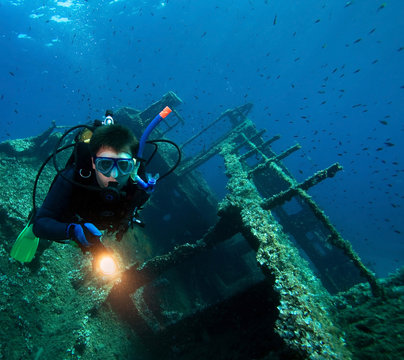 Scuba diver with underwater light around wreck