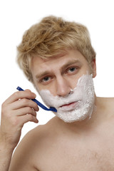 Blonde man shaving face in bathroom, portrait