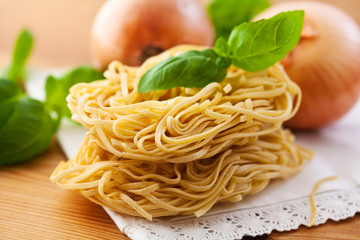 Raw pasta with fresh basil and onion in background