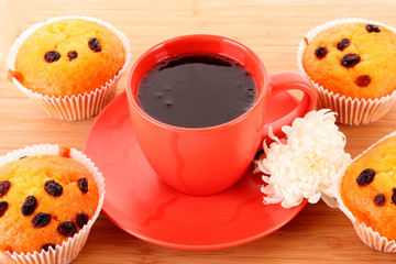 Muffins with raisins and red cup on wooden surface