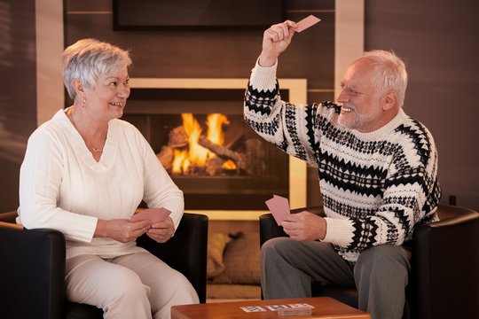 Retired couple playing cards in front of fireplace