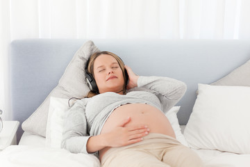 Naklejka premium Relaxed future mom listening to the music on a bed
