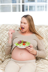 Pregnant woman devouring a salad in the sofa