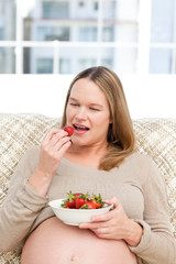 Hungry pregnant woman eating strawberries sitting in the living-