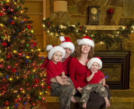 Family of four with santa hats sits beside christmas tree
