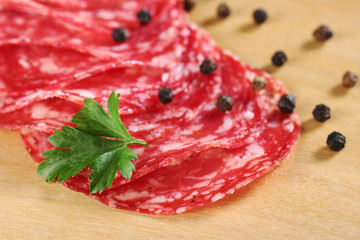 Salami slices with parsley leaf on top and black pepper corns