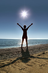 Woman stands on socks ashore opposite sun, heaving up hands up