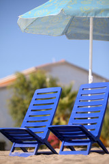 Two dark blue empty chairs stand  under  beach umbrella
