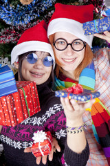 Two beautiful girls with gifts in christmas hats near christmas