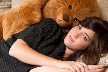 Young woman embracing teddy bear lying on on sofa close-up