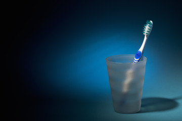 Tooth brush in matte plastic glass over dark blue background. - 28028616